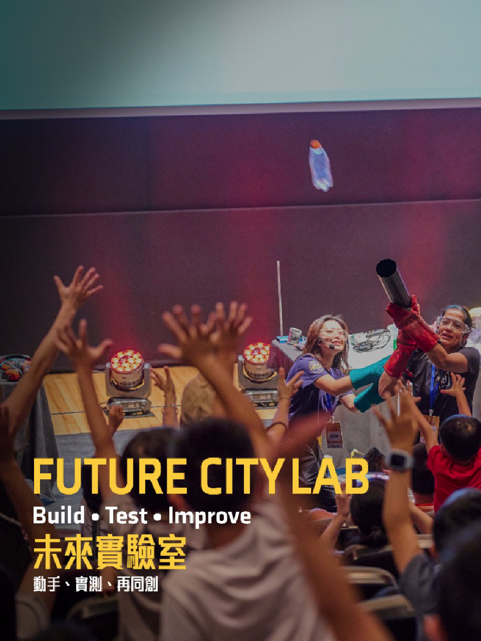 Children raise their hands as the facilitator demonstrates a science experiment with a launcher.