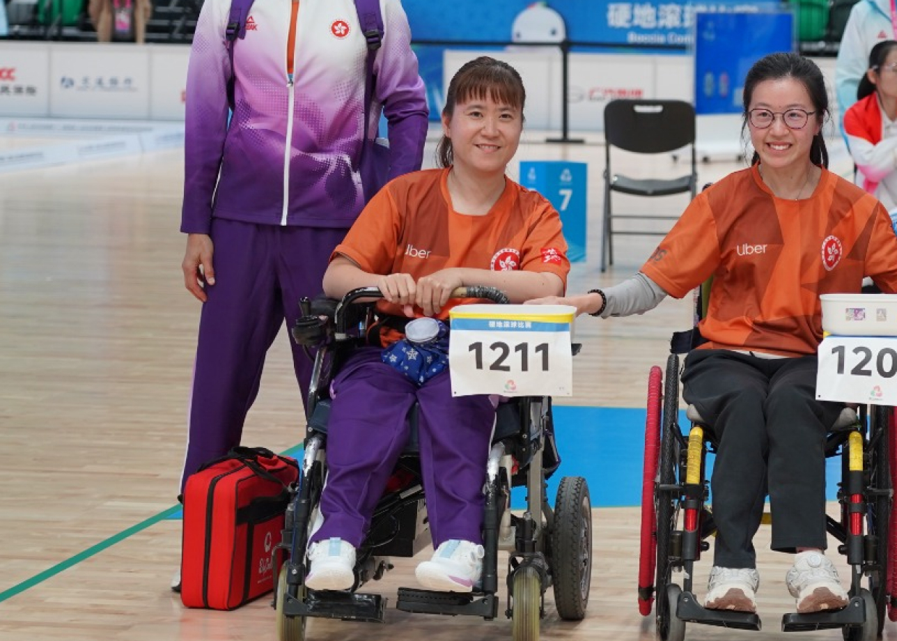 Sharing a proud moment on court, Karen Kwok smiles for a photo in her wheelchair beside her coach in their team uniform.